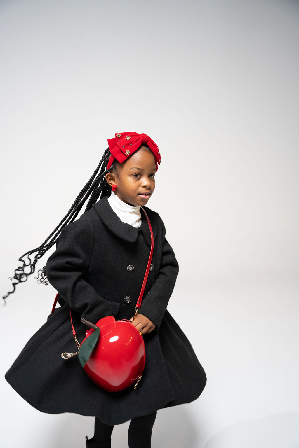 Young girl wearing red jeweled velvet bow headband with black coat and red apple bag