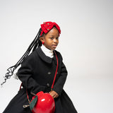 Young girl wearing red jeweled velvet bow headband with black coat and red apple bag