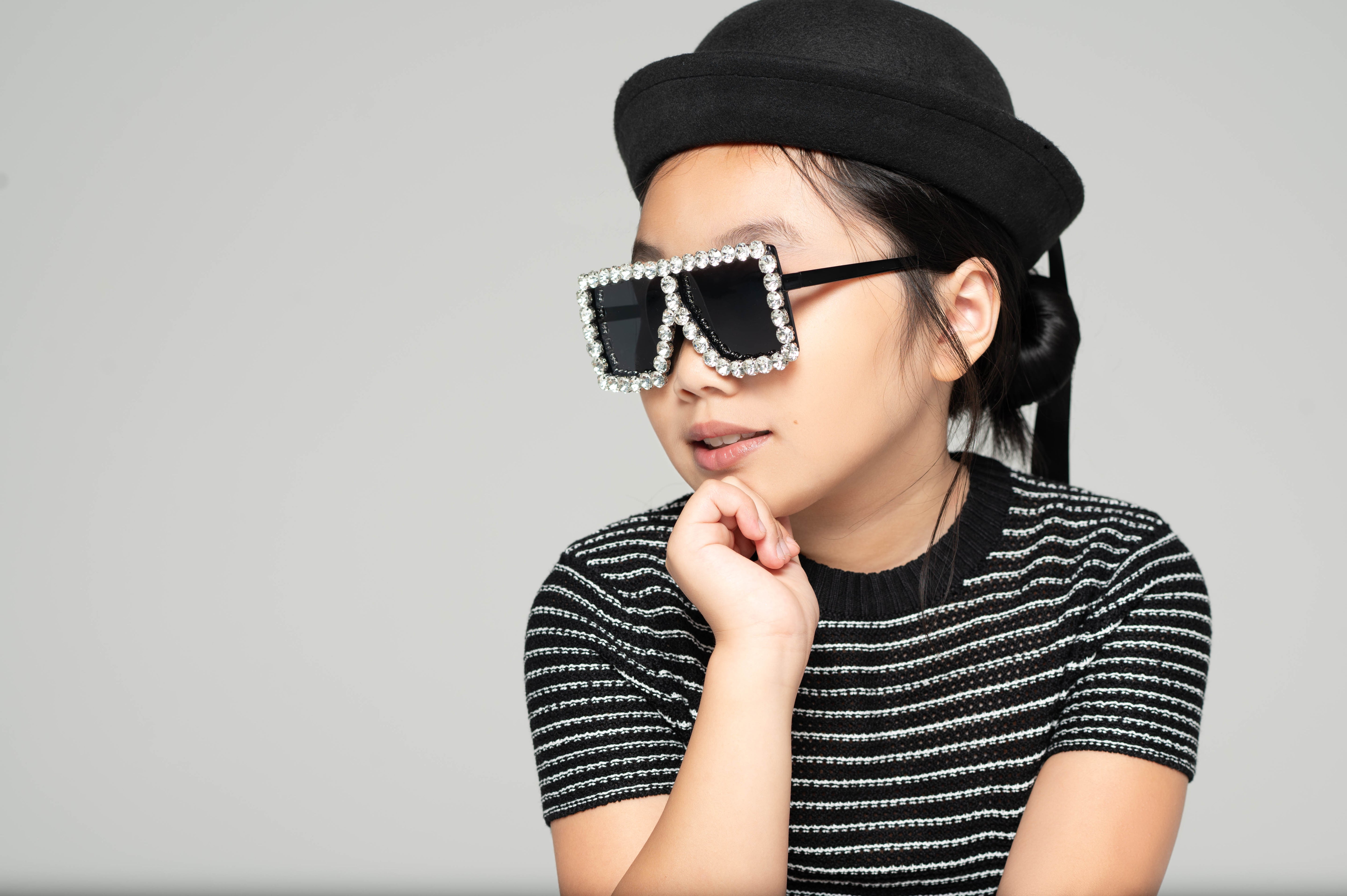 Child wearing Square Diamond Frame Sunglasses in black with a black hat and striped shirt
