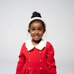 Young girl smiling in red dress with beaded pearl headband in a close-up shot