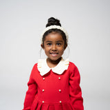 Young girl smiling in red dress with beaded pearl headband in a close-up shot