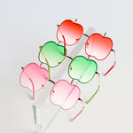 Five pairs of apple-shaped kids sunglasses in red, pink, and green on a clear acrylic stand
