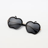 Gala Princess sunglasses in black with gold arms and apple silhouette, laid flat on white surface
