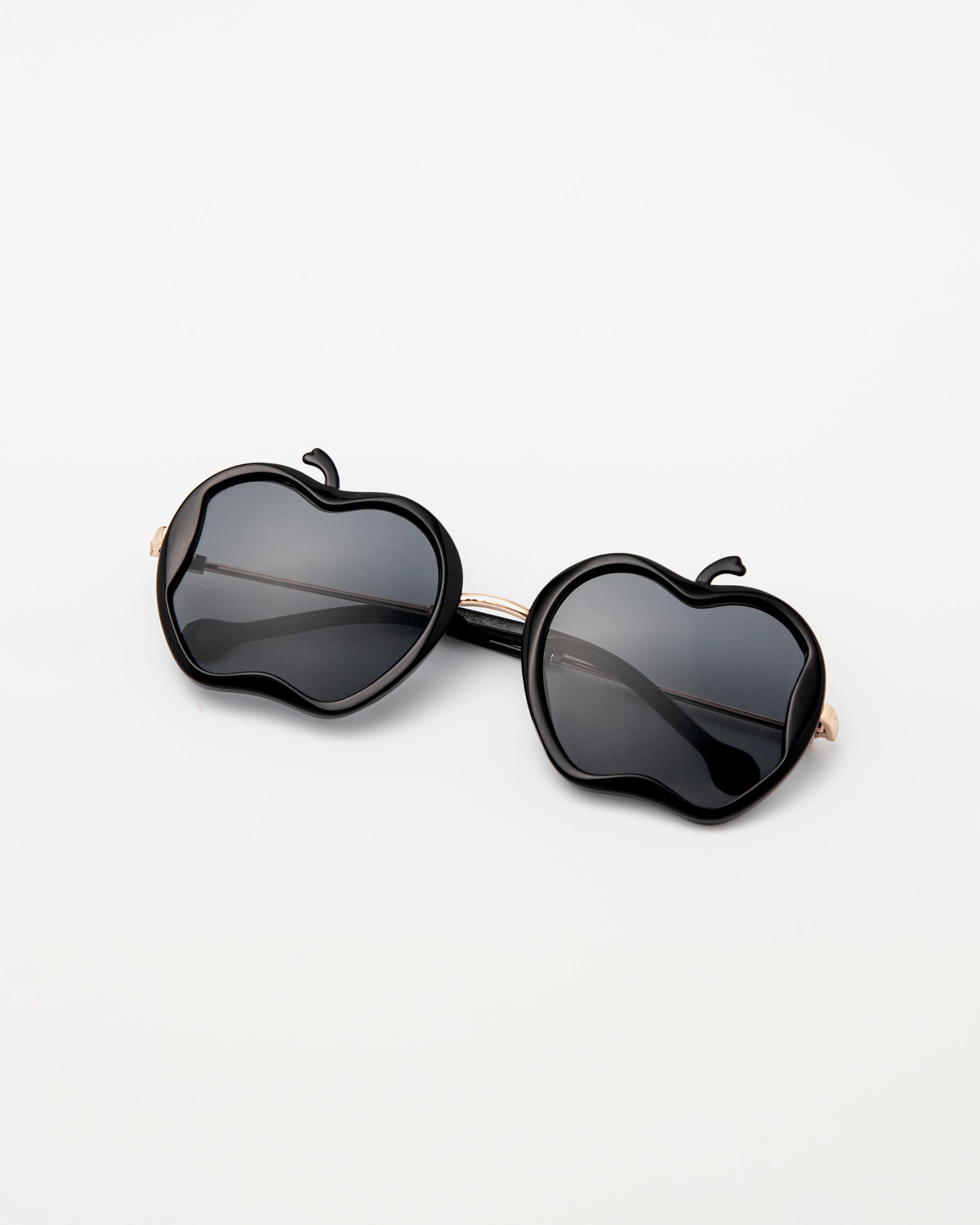 Gala Princess sunglasses in black with gold arms and apple silhouette, laid flat on white surface