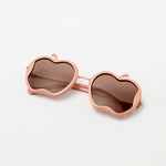 Nude pink Gala Princess sunglasses with apple-shaped frames laid flat on white background
