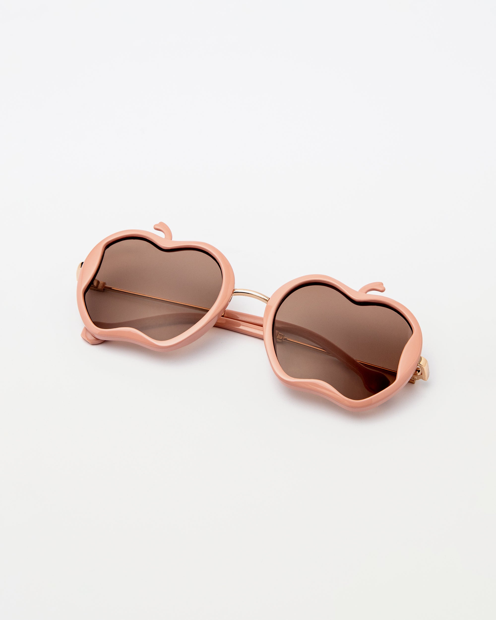 Nude pink Gala Princess sunglasses with apple-shaped frames laid flat on white background