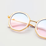 Close-up of Goddess Cream sunglasses with pink and blue gradient lenses, gold frames, and white trim