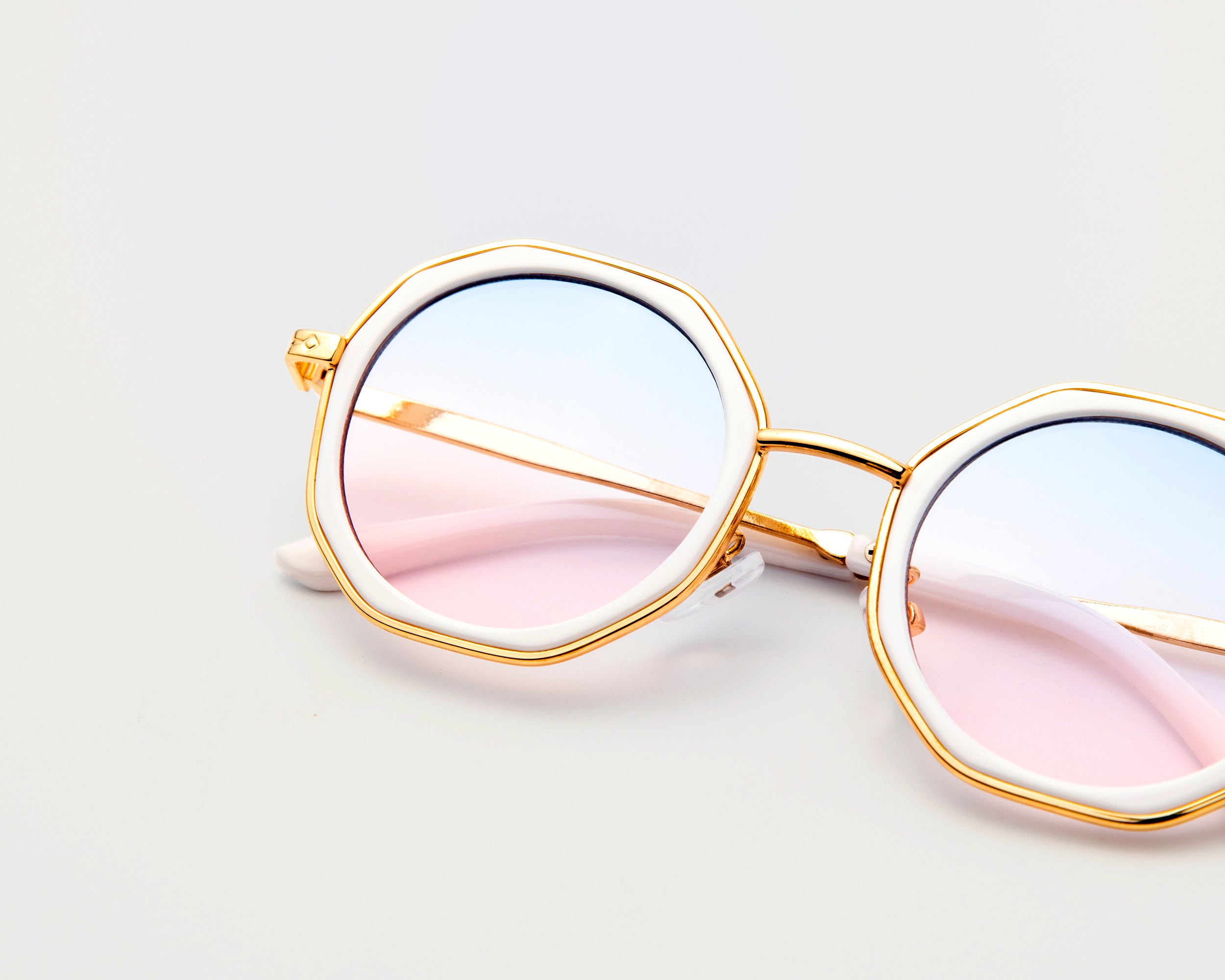 Close-up of Goddess Cream sunglasses with pink and blue gradient lenses, gold frames, and white trim