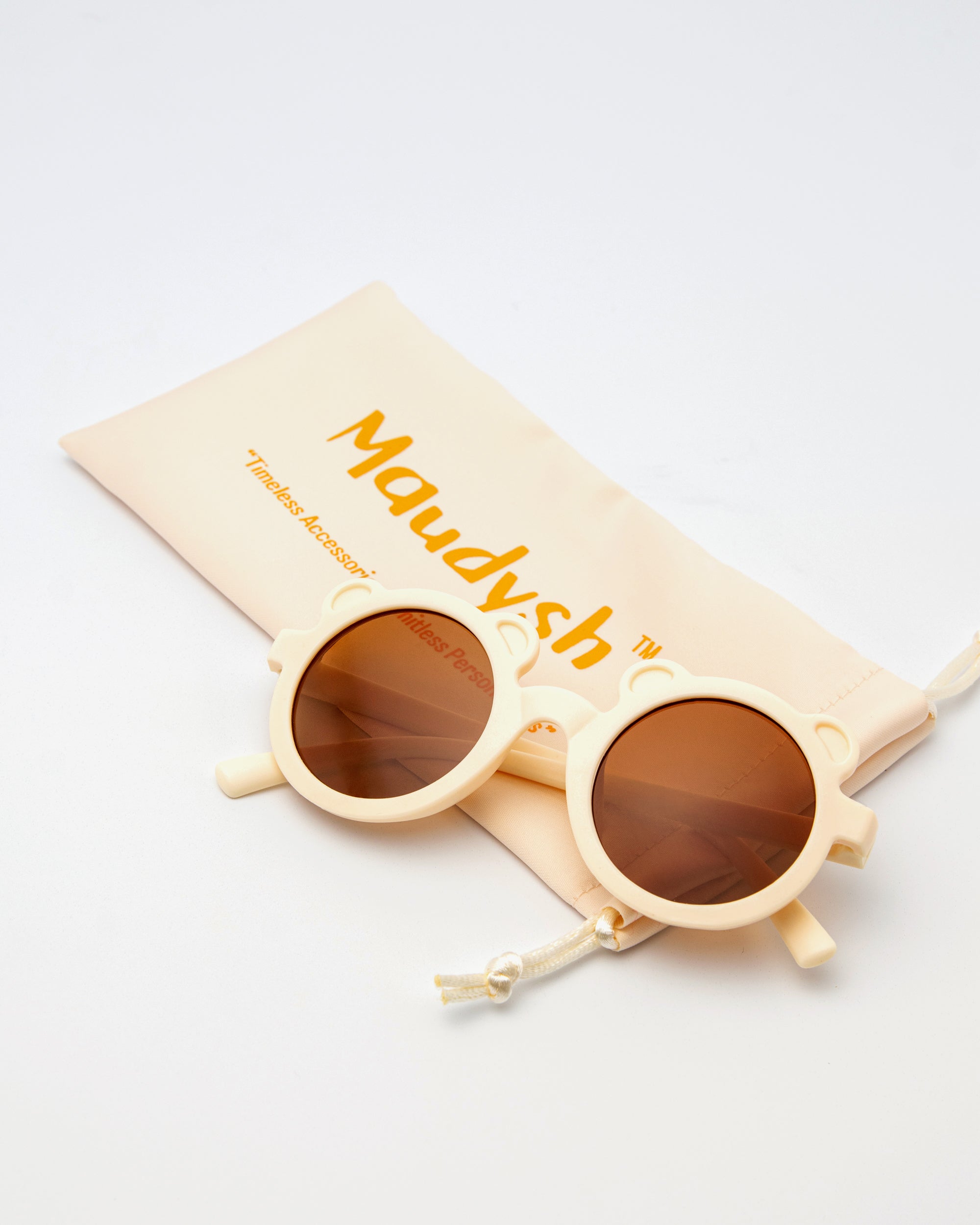  Little Miss Beary Glasses in cream with round lenses, displayed next to peach Maudysh drawstring pouch