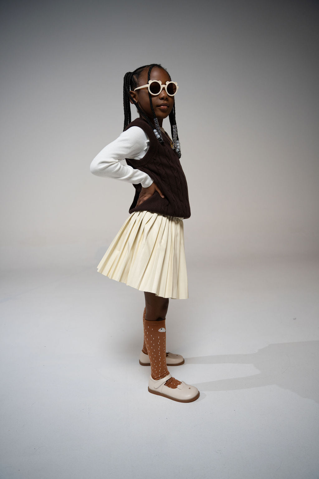 Girl in side profile pose wearing Little Miss Beary Glasses, styled with cream pleated skirt and brown vest