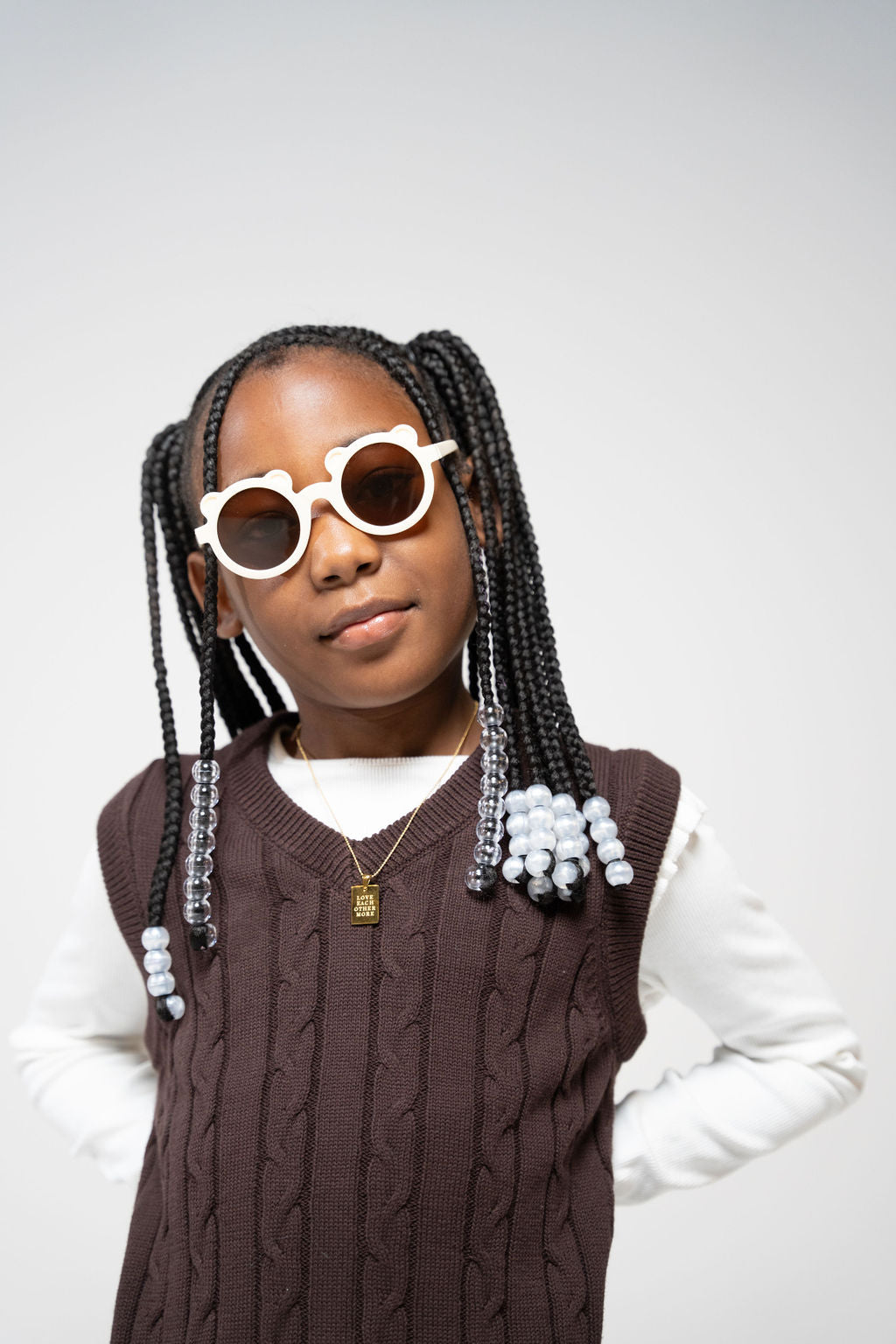 Close-up of a girl wearing Little Miss Beary Glasses with braids, brown vest, and gold layered necklaces