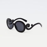 Noirette Sunglasses with black oval frames and statement curved arms, displayed against white background