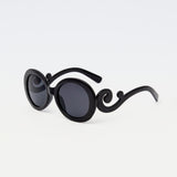 Noirette Sunglasses with black oval frames and statement curved arms, displayed against white background