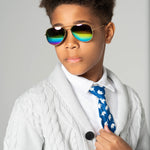 Boy wearing Rainbow Gleam sunglasses with gold frames and reflective rainbow lenses, styled in a white shirt and knit cardigan