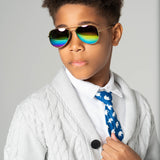 Boy wearing Rainbow Gleam sunglasses with gold frames and reflective rainbow lenses, styled in a white shirt and knit cardigan