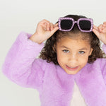 Girl smiling while lifting Sparkle Lilac Blooms sunglasses, wearing a lilac faux fur jacket
